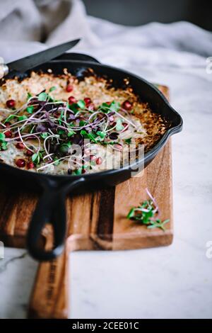 Scrambled eggs with herbs in black iron frying pan on wooden†cutting board with knife on desk†covered with white textile material in soft focus Stock Photo
