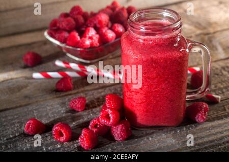 Healthy appetizer red raspberries fruit smoothie in a glass jar with berries background, top view. Detox and antioxidant drink. Vintage style. Stock Photo