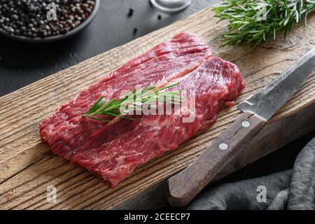 Raw marbled ribeye steak with rosemary sprig on woden cutting board. Close up. Stock Photo