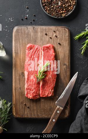 Raw marbled ribeye steak with rosemary sprig on cutting board. Vertical composition. Stock Photo