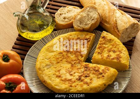 Spanish tortilla with tomatoes, garlic, bread, onions and a glass jar of olive oil on a light background Stock Photo