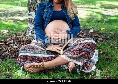 Pregnant attractive Woman sitting under tree Stock Photo