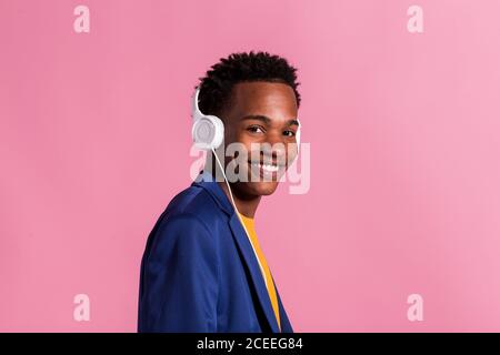 Side view of young black man in colorful purple jacket and?with headphones smiling at camera on pink background Stock Photo