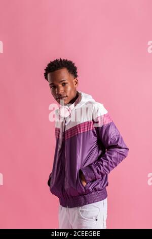Young black man wearing modern trendy sportive jacket with headphones and looking at camera on pink background Stock Photo