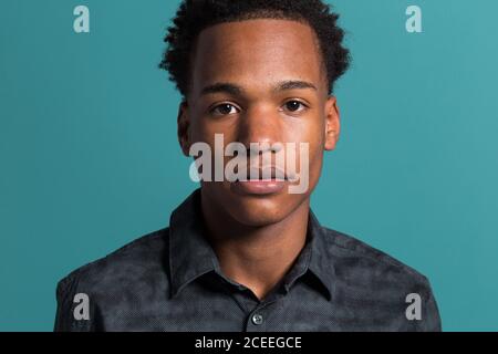 Crop portrait of young African-American serious man in shirt looking at camera on blue background Stock Photo