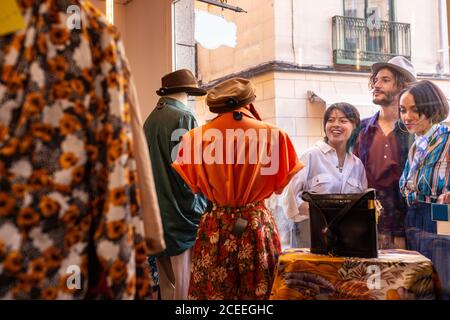 Young man and women smiling and looking at clothes inside small store while standing on street near display window Stock Photo