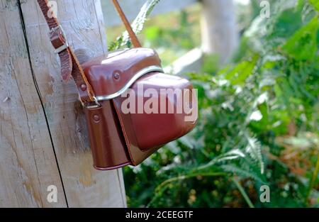 brown leather vintage camera case hanging from post in countryside scene, norfolk, england Stock Photo