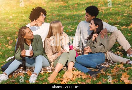 Young cheerful friends having picnic in forest, drinking coffee Stock Photo