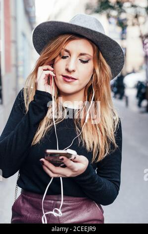 Young blonde Woman listening music with earphones of her mobile phone in Madrid streets, Spain Stock Photo