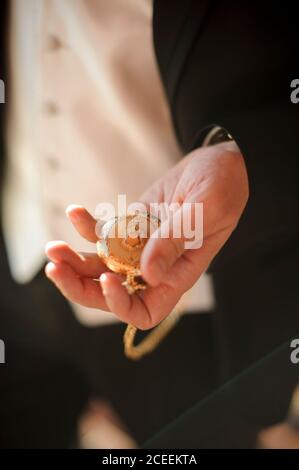 Crop unrecognizable man in suit standing and watching time on pocket watch. Stock Photo