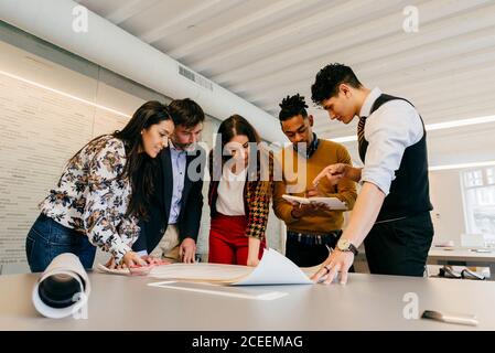 Multiethnic office team standing at the table while working on the blueprint. Stock Photo