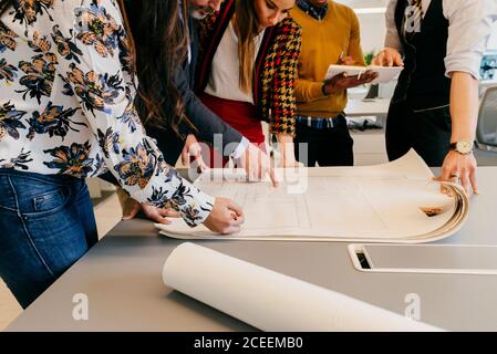 Crop unrecognizable multiethnic office team standing and working at blueprint on the table. Stock Photo