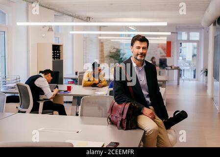 Handsome adult man sitting on table in office Stock Photo