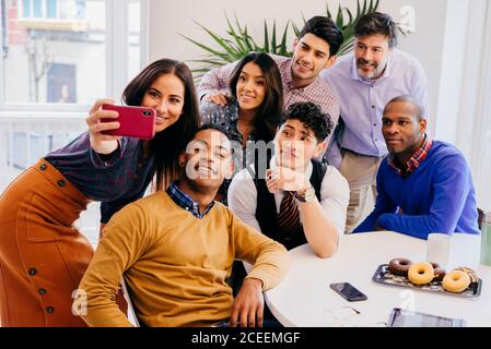 Multiracial team standing and sitting while taking selfie at the table in office. Stock Photo