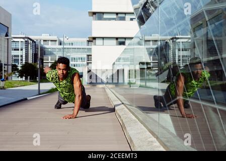 Adult ethnic man doing push-ups exercise with one arm while working out on city street Stock Photo