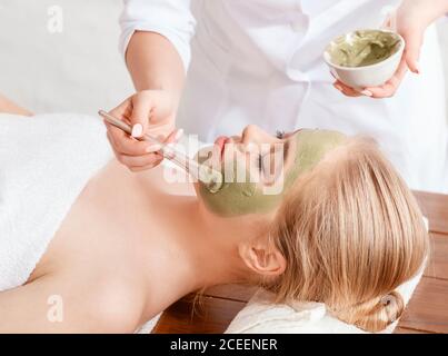 Facial and beauty. Beautician smears client face with clay Stock Photo