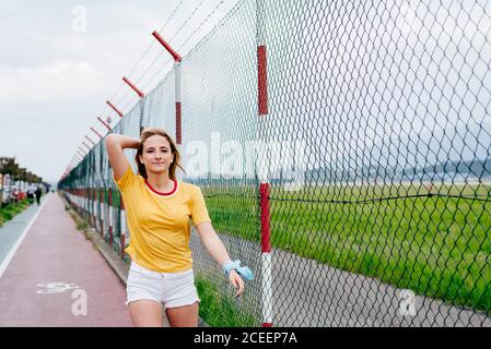 Casual teen girl in shorts and roller skates standing on lane of sports ground looking at camera. Stock Photo