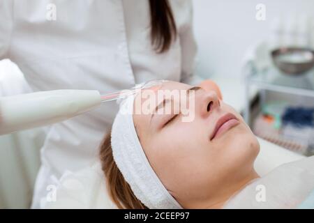 A professional cosmetologist performs a Darsonvalization procedure at the spa. Beautiful caucasian woman on a cosmetic procedure. health Center Stock Photo