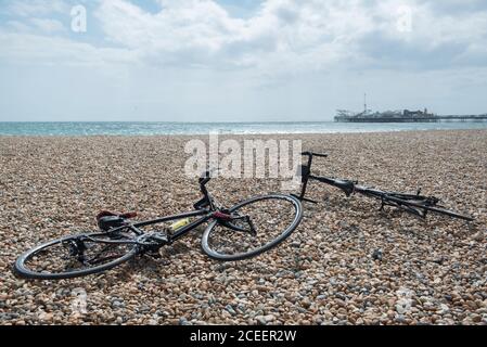 Two bike lie on Brighton's pebble beach with the Brighton Pier and sea behind. Stock Photo