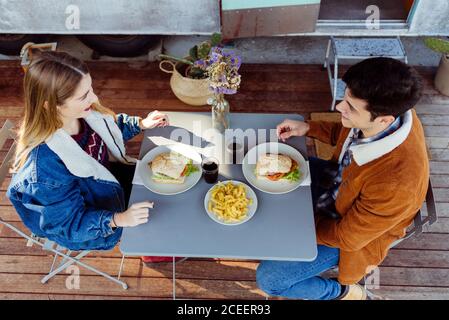 Side view of young man and Woman smiling and looking at each other while having delicious romantic dinner near shabby caravan Stock Photo
