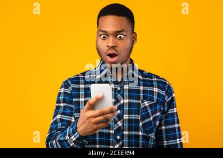 Shocked Black Man Looking At Smartphone Reading SMS, Yellow Background Stock Photo