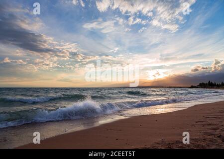 Beautiful sunset by the lake. Bright clouds are reflected in the water. Kyrgyzstan. Stock Photo