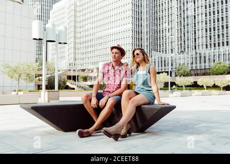 Young man and Woman sitting and relaxing on modern bench on city street Stock Photo