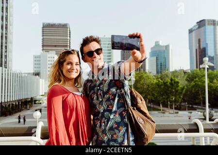 Young man and Woman standing at handrail and taking selfie on city street Stock Photo