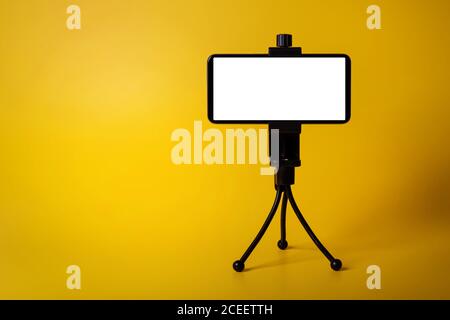 mobile phone mounted on mini tripod with blank screen isolated on yellow background. copy space Stock Photo