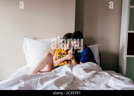 Cheerful young man and Woman lying and cuddling in bed at home. Stock Photo
