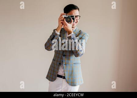 Cheerful handsome man in casual jacket taking photos at beige wall. Stock Photo