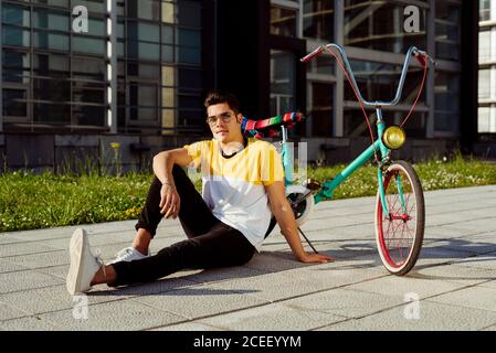 Young man sitting on pavement near vintage bicycle Stock Photo