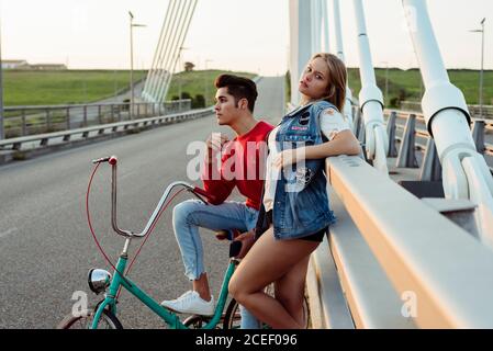 Attractive young couple standing on bridge with vintage bicycle leaning on railing Stock Photo