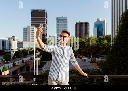 man leaning on fence and taking selfie with smartphone Stock Photo