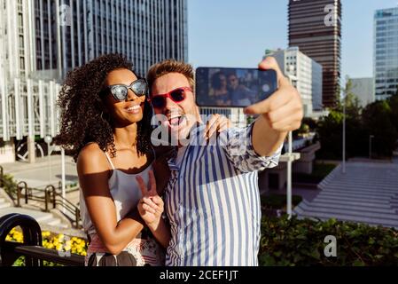 Beautiful black Woman and handsome Caucasian man posing for selfie while standing on background of modern city Stock Photo