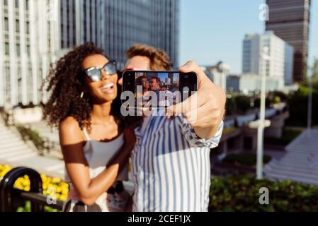 Beautiful black Woman and handsome Caucasian man posing for selfie while standing on background of modern city Stock Photo