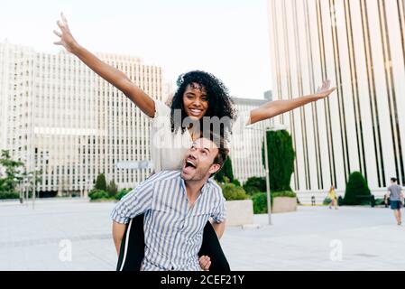 Handsome Caucasian man giving piggyback ride to African-American Woman while having fun on city street together Stock Photo