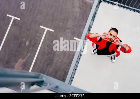 From above of cool young man wearing casual clothes standing on roof looking at camera Stock Photo