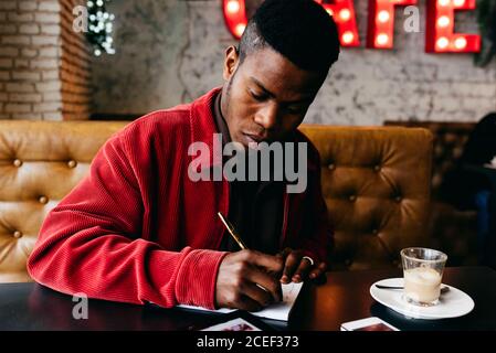 Serious african male in red jacket letter at table in cafe Stock Photo