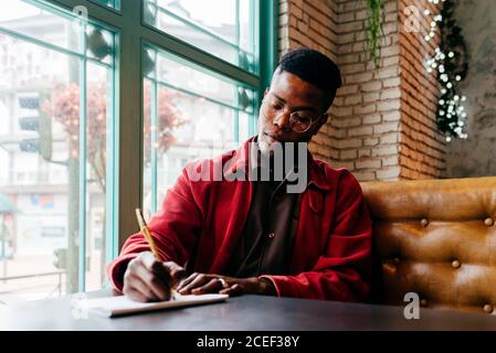 Serious african male in red jacket letter at table in cafe Stock Photo