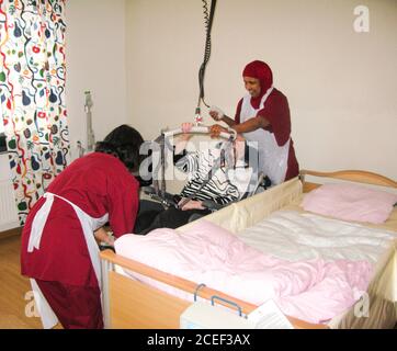 Old women get help from the accommodation staff to be moved from the wheelchair to the bed by lift Stock Photo