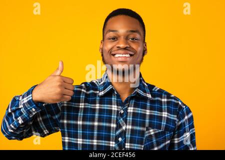 Positive African Man Gesturing Thumbs-Up Standing Over Yellow Background Stock Photo