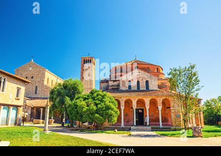 Church of Santa Fosca building on Torcello island, Cathedral of Santa Maria Assunta with bell tower campanile, blue clear sky background. Venetian Lagoon, Veneto Region, Northern Italy. Stock Photo