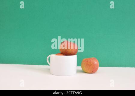 Apples in a white cup with a apple isolated on green background separation concept Stock Photo