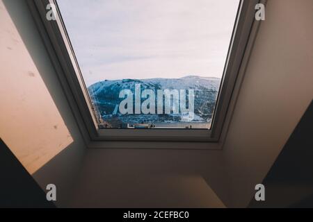 Landscape of snowy mountains through glass window in mansard roof in sunlight Stock Photo