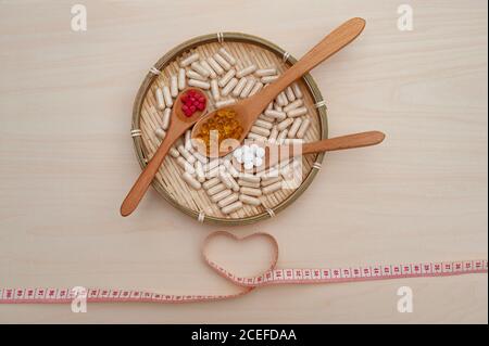 Healthy lifestyle - Vitamins, minerals and nutritional supplements in wooden spoons inside a braided bamboo plate with a heart shaped soft vinyl tape Stock Photo