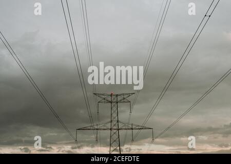 Minimalist view of black wires and high voltage power pole on background of dark cloudy sky. Stock Photo