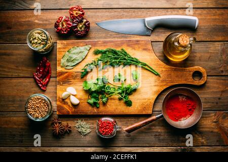 From above various spices and bottle of oil placed on timber tabletop near sharp knife Stock Photo