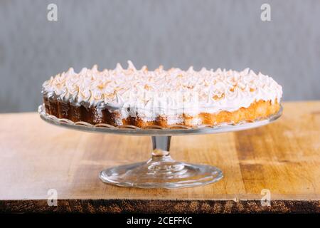 Crispy tart topped with baked white fluffy meringue and served on glass cake stand on table Stock Photo