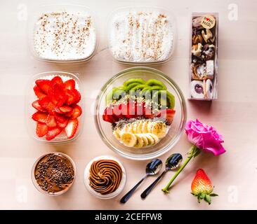 Flat lay of arranged sweet desserts and healthy fruit bowl on table with rose. Stock Photo